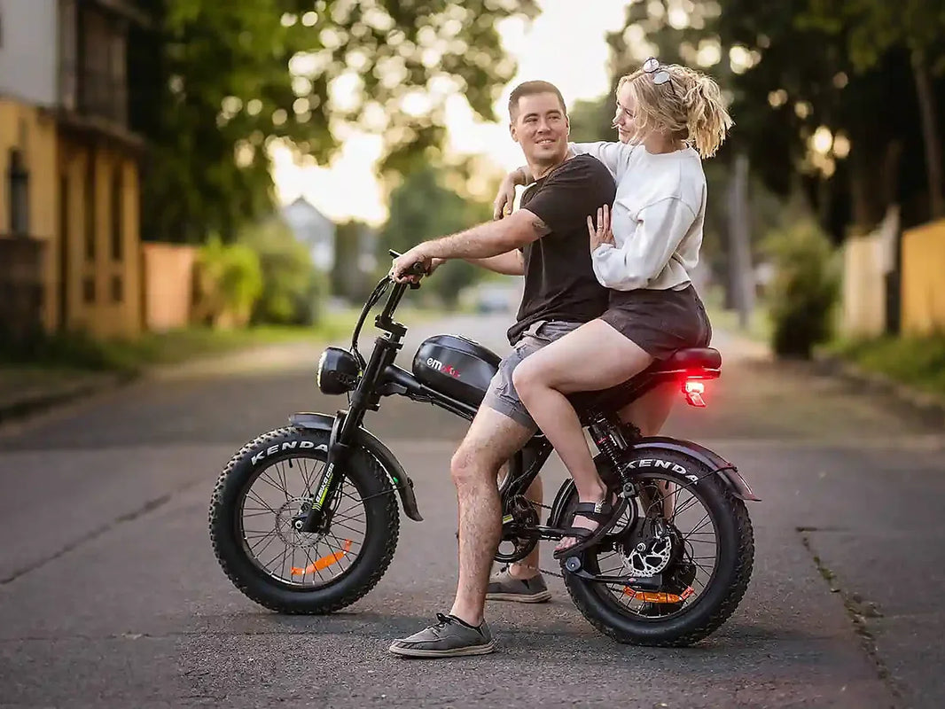 A couple riding the EMOKO C93 dual-seat electric bike on a quiet neighborhood street at sunset