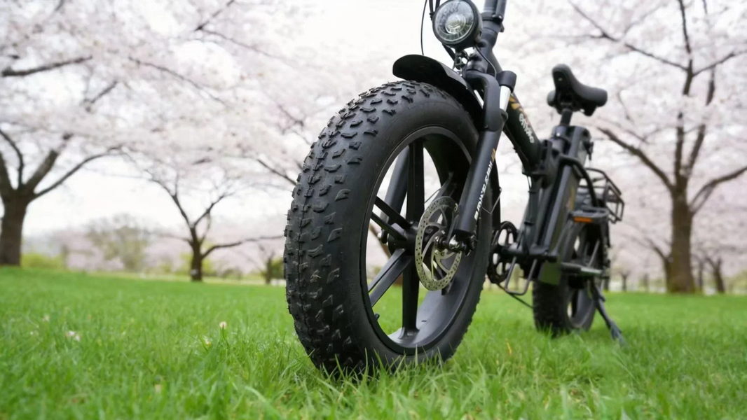 Emoko fat tire electric bike parked on fresh green grass under blooming cherry blossom trees, illustrating the 2026 spring e-bike maintenance and revival guide.