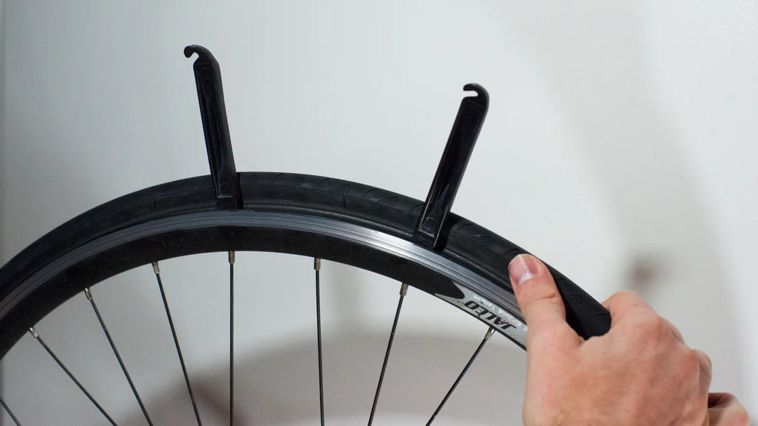 Hands removing a bicycle tire bead from its rim during inner tube puncture repair