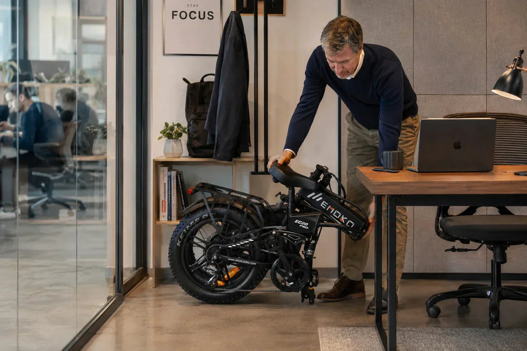 Folded EMOKO EC20 e-bike being placed beside an office desk, showing practical storage in a workspace.